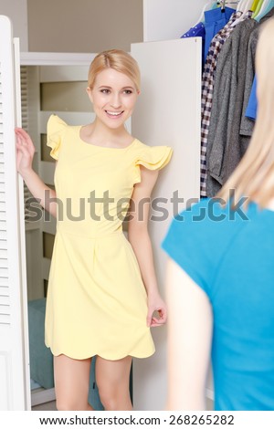 Festive look. Close-up of a young smiling blonde teenage girl trying yellow dress in a dressing room and demonstrating her look to her friend