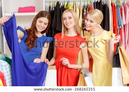 Deep blue. Three female shoppers holding paper bags and looking at a dark blue skirt with clothing rack on a background