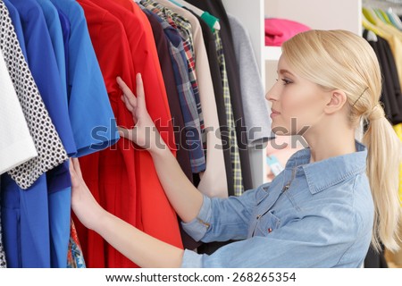 Big sale. Smiling female shopper choosing dress at clothing rack in a retail store