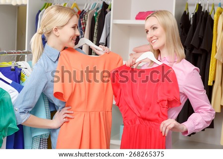 Wide range of fashionable dresses. Nice blond sales consultant and a female shopper trying dresses of different colors and smiling to each other