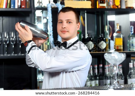 Barman job. Young handsome barman mixing cocktails in shaker at the bar