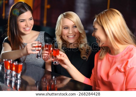 Let the party start. Three smiling young women toasting with shots at the bar