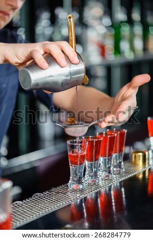 Mixing cocktails. Close-up of barman with cocktail shaker pouring red alcoholic drink into glasses in bar
