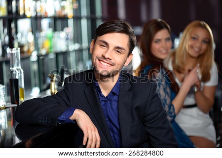 Handsome guy. Young man smiling to the camera while two girls in blurry are looking at him with interest