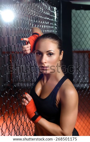Pure seduction. Young fit attractive sports woman with boxing bandages on her hands hanging on a fighting cage in a gym