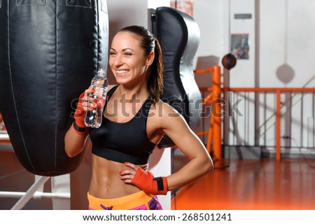 Healthy and fit. Young cheerful woman drinking water in a boxing gym and contagiously laughing