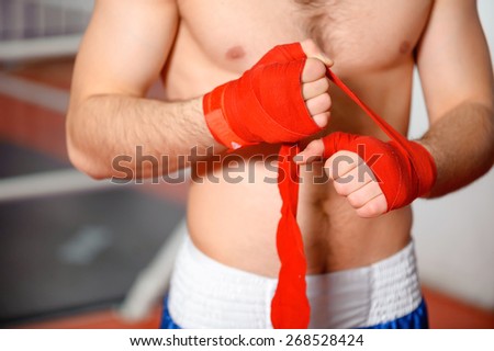 Boxing bandage. Close up of a sportsman binding red boxing bandage in a gym