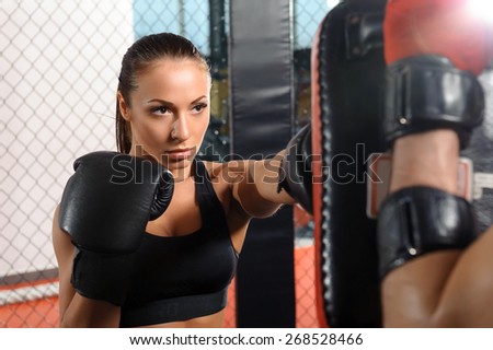 Female boxer. Young beautiful sportswoman striking a punching pad in a boozing ring