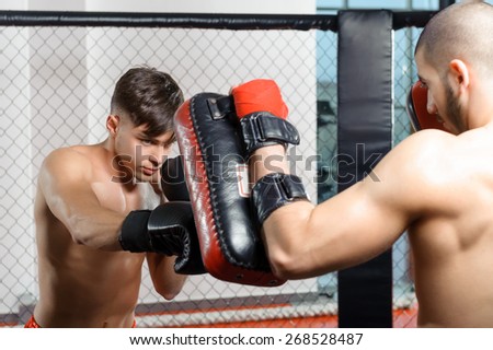Coaching. Boxer and his coach doing some sparring in the ring with the help of a punching pad