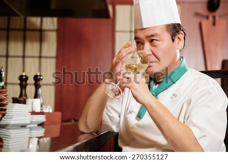 Tasting wine. Japanese cook sipping white wine at kitchen counter