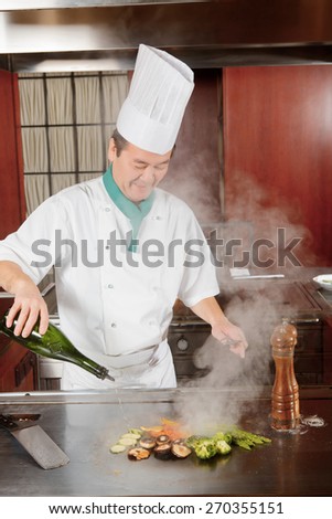 Spice cuisine. Japanese cook in uniform pouring sauce on fried vegetables on hot oven