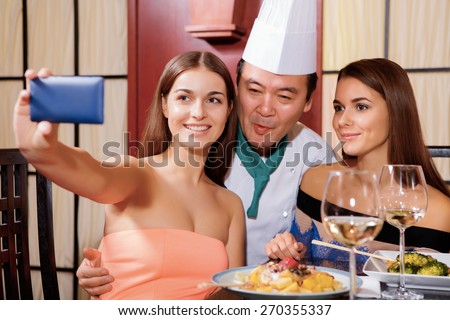 Photo to remember. Two beautiful smiling women doing selfie with a Japanese chef-cook in a restaurant