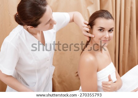 Great job done. Beautician examining the face of a young brunette woman wearing a towel in spa center