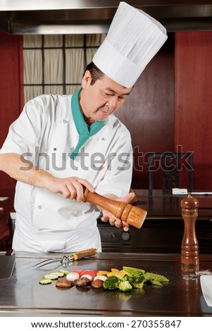 Salted vegetables. Japanese cook in white uniform salting fried vegetables on a table