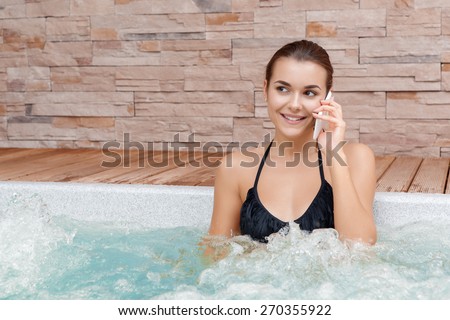 Joyful conversation. Young smiling woman talking over the phone bathing in jacuzzi in a spa center