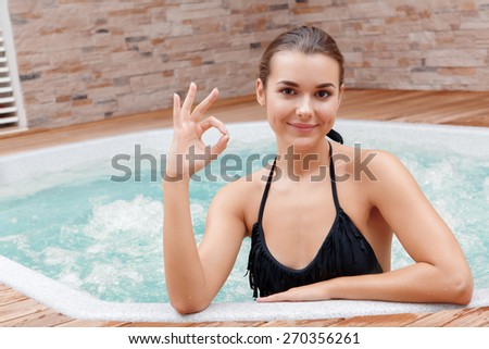 Just perfect time. Young beautiful woman showing sign ok when bathing in a jacuzzi