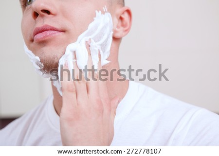 Spread over. Handsome young guy standing in front of mirror and spreading over shaving gel.