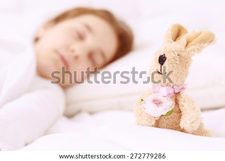 Little guardian. Pretty little red-haired girl sleeping with her favorite toy on white bed.