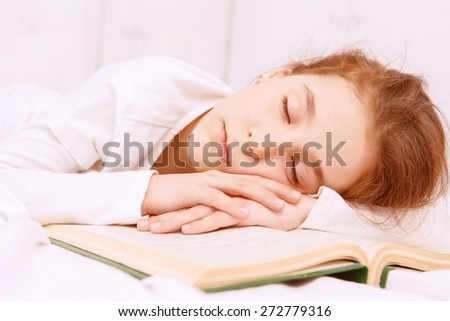 Very interesting book. Cute little red-haired girl sleeping on desk on. opened book