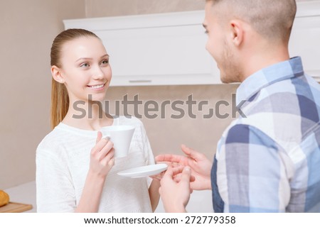 Listen carefully. Two beautiful young people standing in kitchen drinking coffee and listening to each other.