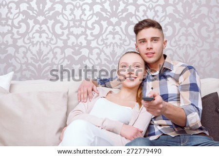 Lets watch TV. Young beautiful couple sitting on white sofa and changing tv channels