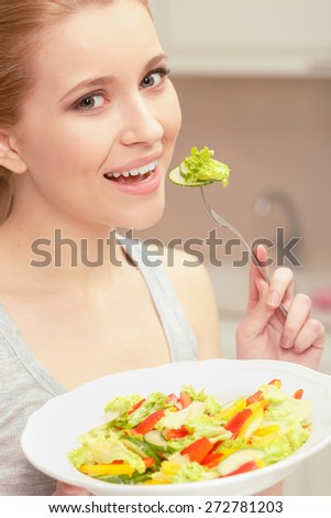 Pleasant lunch. Close-up of a young lady holding plate with salad and tasting a piece of cucumber with fork