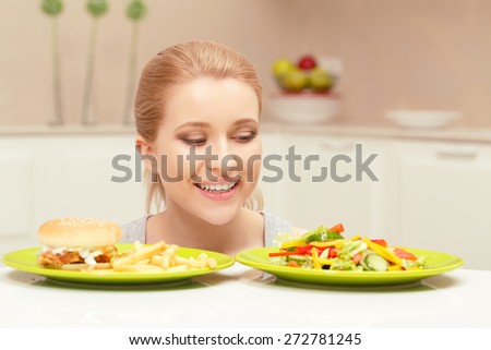 Made right choice. Close-up of a smiling lady who decided to eat vegetables but not fast-food looking at plate with salad