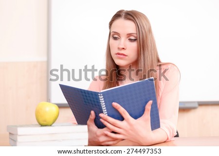 Compulsive work. Young-looking woman looking upon blue copy book on background of white blackboard