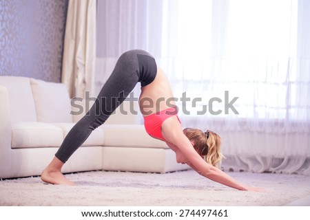 Awake sense. Young woman leaning forward in yoga pose indoors in white decorated living room.