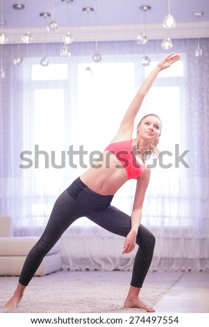 Keep fit. Pretty young lady doing stretching at home in white decorated living room.