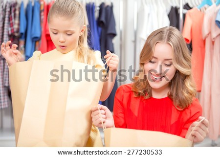 Happy shopping. Young mother and her small daughter looking happily inside packages with new clothes in a fashion store