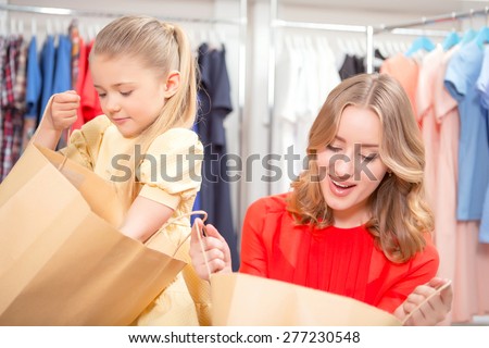 Happy shopping. Young mother and her small daughter looking happily inside packages with new clothes in a fashion store