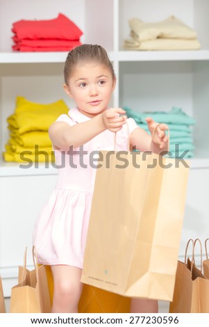Small happy girl stretching her hands with the packages with a new dress in a fashion store