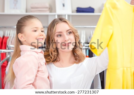 Family shopping. Young mother choosing yellow dress with her daughter ,both smiling