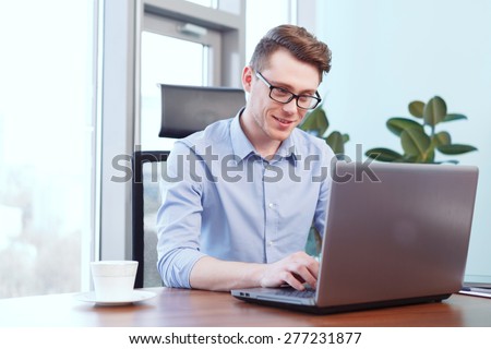 Office work. Young smiling businessman sitting at desk and working on computer in office.