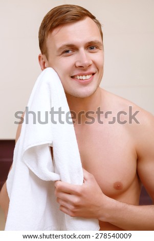 Daily routine. Young looking handsome man wiping his face with towel