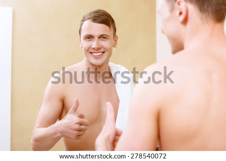 Thumbs up. Smiling topless man with thumb-up in front of mirror in bathroom.