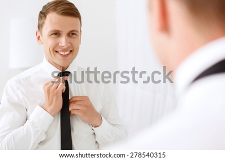Making beautiful. Smiling handsome man fixing his tie in front of mirror.