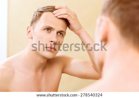 Furbishing up. Topless young man fixing his hair in front of mirror.