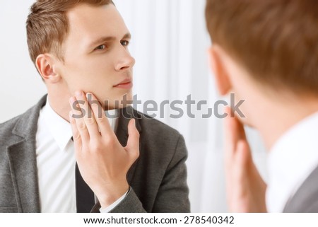 Intent glance. Handsome young man looking in mirror and checking his bristle hair on face.