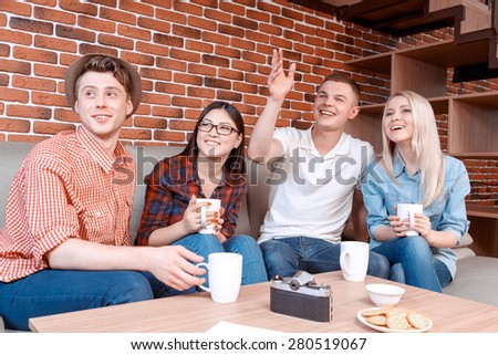 Ready to make an order. Young handsome boy calling a waiter sitting in a cafe with his friends drinking coffee and smiling, brick wall on the background