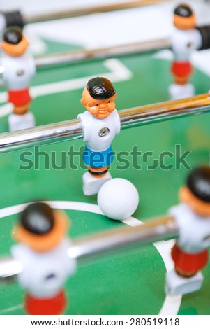 Close up of figure of table hockey on a green play-field and a white ball selective focus