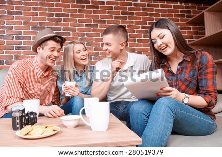 Happy meeting. Young smiling girl writing in a notebook while her friend laughing discussing something funny drinking tea, camera cookies and cups on the table