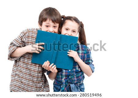 Hide and seek. Small pretty girl and her older brother smiling and hiding behind a big blue book isolated on white background