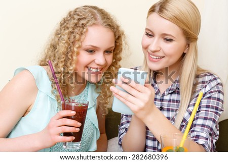 Nice picture. Two attractive smiling ladies sitting in cafe and looking at mobile phone.