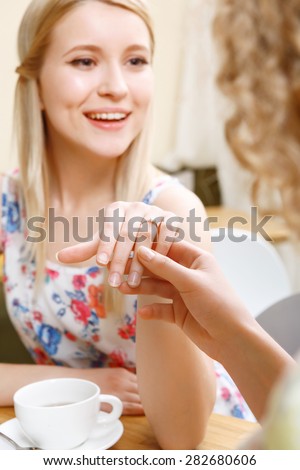 Showing off. Pretty young smiling blond lady showing her wedding ring to friend in cafe.