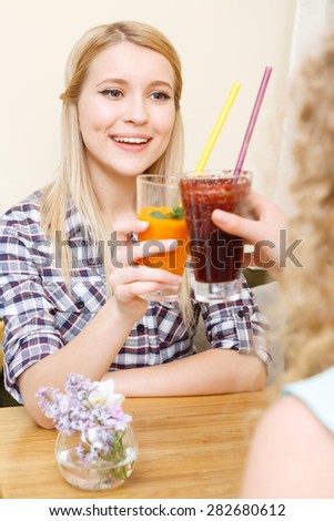 For meeting. Young attractive blond girl clinking glasses with cocktails in cafe.