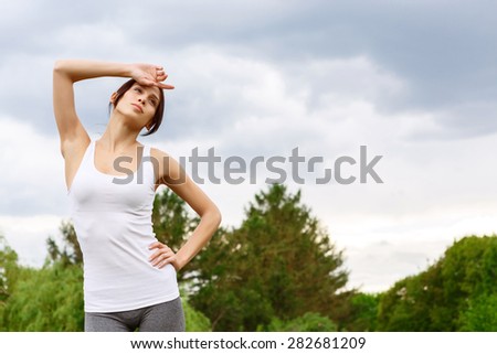 Little bit tired. Attractive young woman in park holding one hand on her waist, and another on forehead