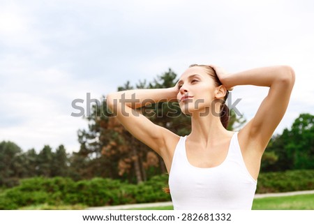Inner harmony. Young beautiful woman standing in park with arms behind her head