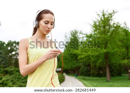 Inspiration with music. Pretty young  sporty lady standing in park with headphones and player